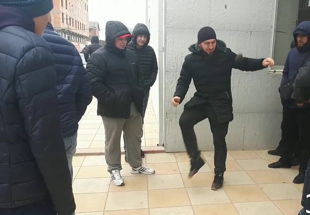 Мужчина подбрасывает лянгу ногой во дворе, вокруг стоят зрители