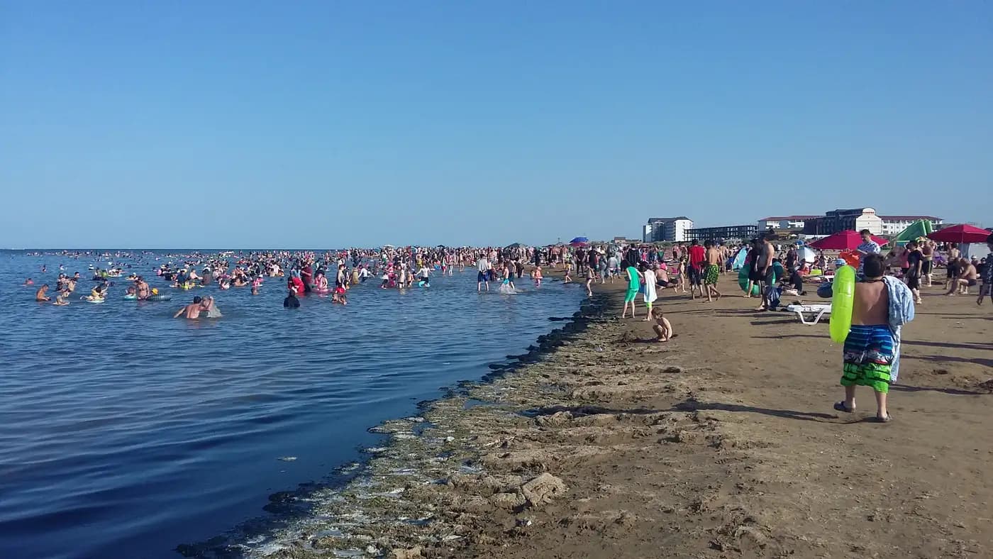 Пляж Избербаша летом: отдыхающие купаются в Каспийском море, на берегу видны городские здания