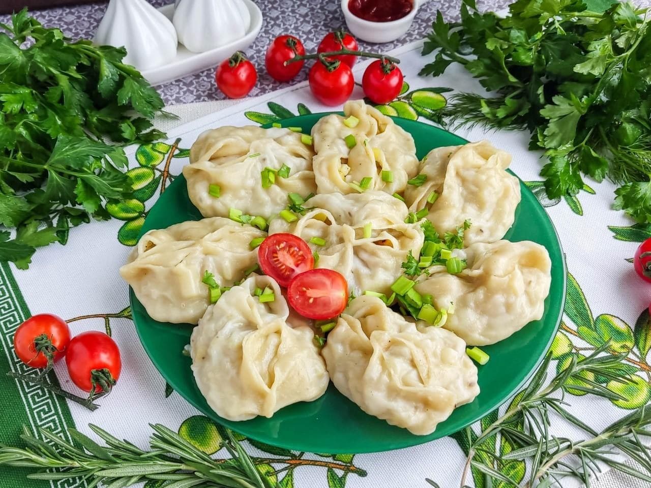 Дагестанские манты на тарелке с зеленью и черри — блюдо из теста с мясной начинкой