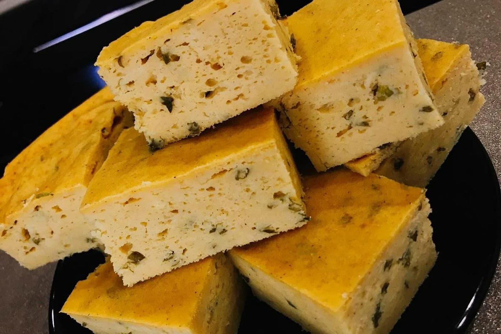 Куски мучари с жареным луком и зеленью в разрезе, выложенные горкой на тёмной тарелке