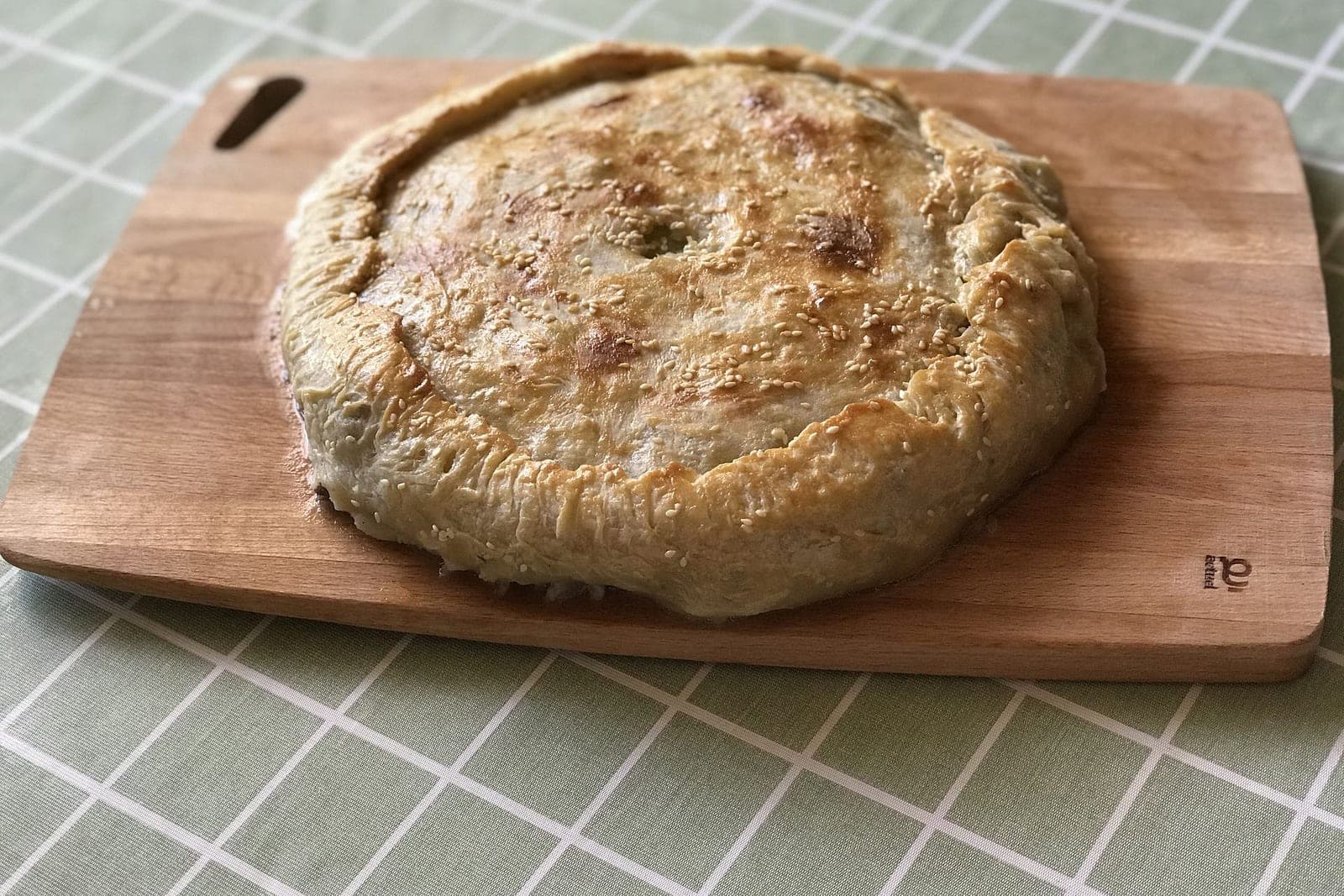 Целый круглый пирог цкан с золотистой корочкой, посыпанный кунжутом, на деревянной доске