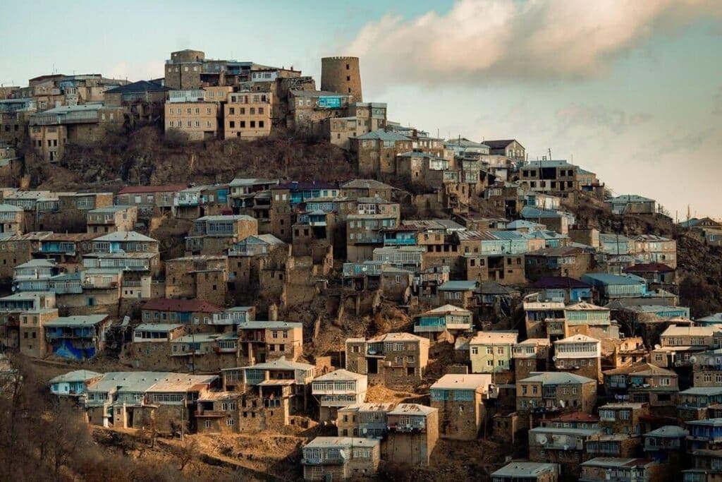 Панорама Кубачи на закате: каменные дома и сторожевая башня на вершине холма среди гор Дахадаевского района