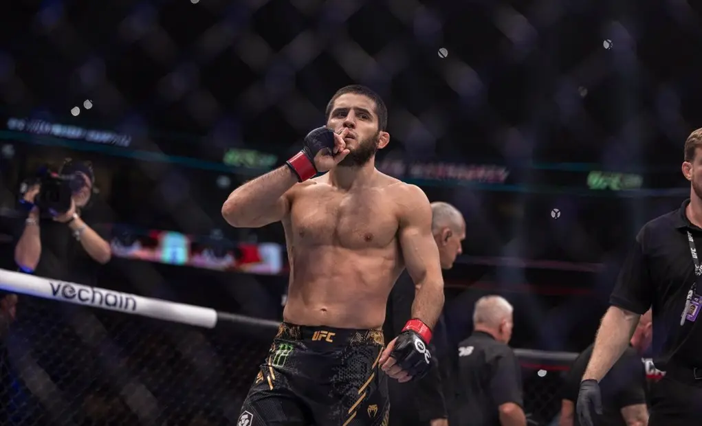 Боец в клетке UFC поднимает руку после победы, вокруг судьи и операторы
