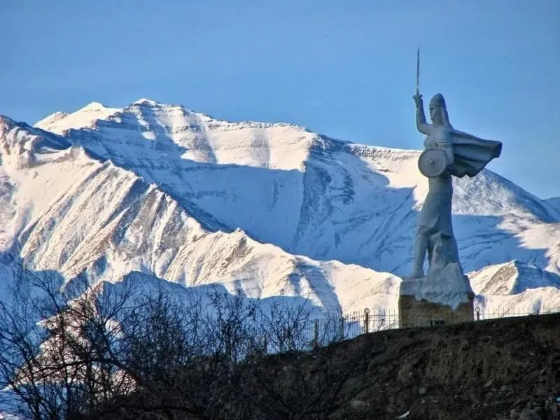 Памятник Парту Патиме зимой на фоне заснеженного горного хребта